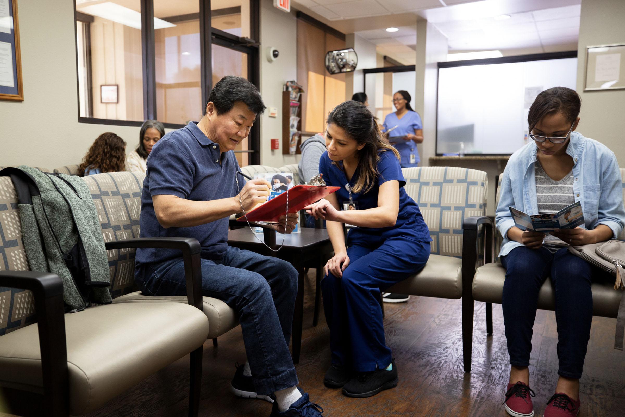 A healthcare working assisting a patient with filling out forms in the waiting room of a medical facility